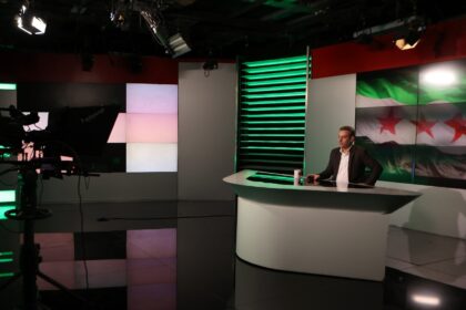 A man delivers a statement in front of the Syrian opposition flag at Syrian state televisi