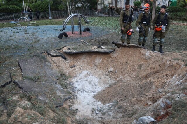 Israeli emergency responders inspect a crater at the site where a projectile fired from Ye