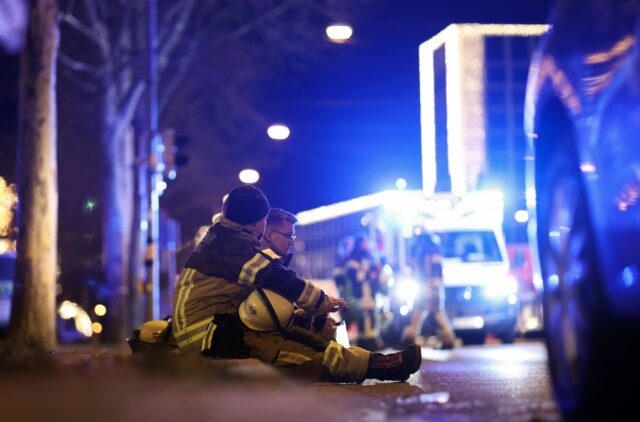 Two rescuers sit on the ground to rest after a car crashed into a crowd at a Christmas mar