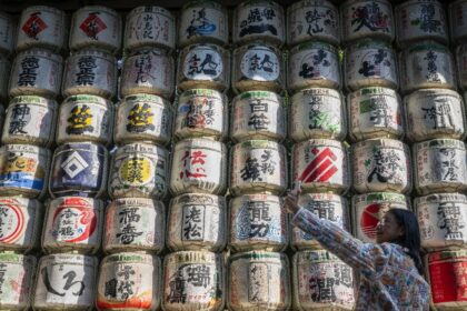 A woman takes a selfie in front of a display of sake barrels at Meiji Shrine in Tokyo