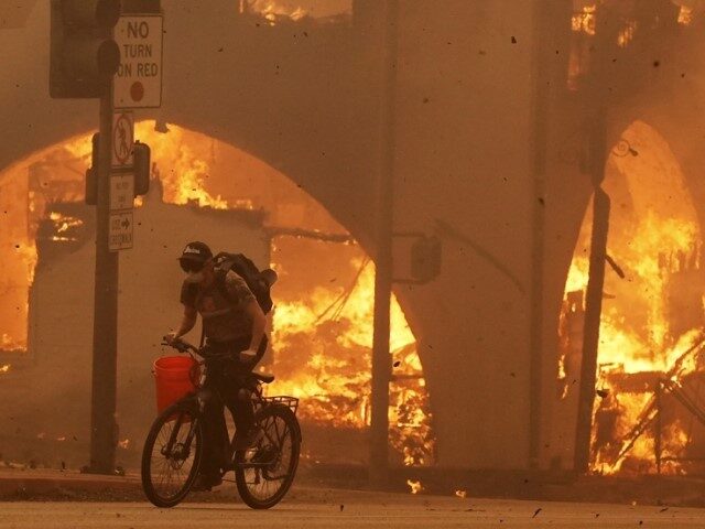 A cyclist pedals past a burning structure on Lake Avenue, Wednesday, Jan. 8, 2025, in the