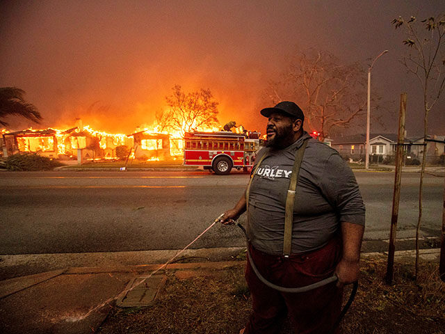 A resident sprays their property with a garden hose as the Eaton Fire engulfs structures a