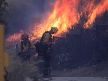 Firefighters work to put out a brush fire burning near homes in Pacific Palisades, Califor