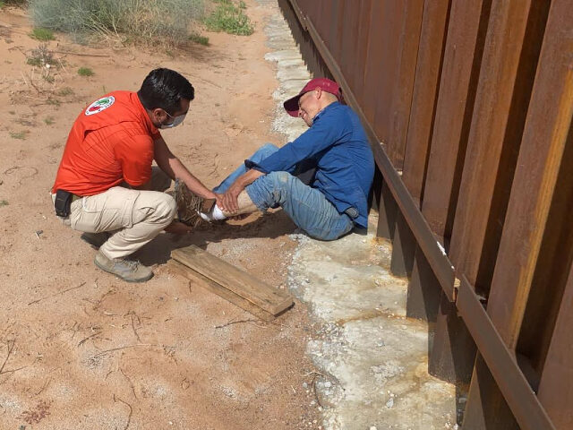 A Mexican official helps a migrant that hurt his leg near the border fence. (Credit INM)