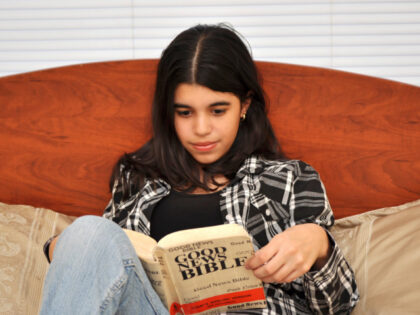 Teen girl reading the Bible sits on the couch and reading the bible at home. (Photo by Rob