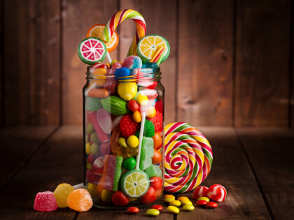 Front view of an open candy jar filled with multi colored candies, lollipops and jelly bea