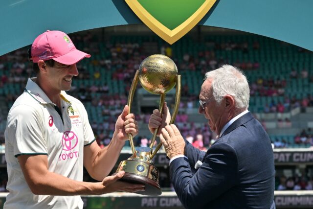 Australia’s captain Pat Cummins (L) is handed the Border-Gavaskar Trophy by Allan Border