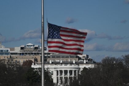 The US flag flies at half-staff on the National Mall, with the White House in the backgrou