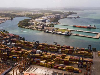 Cargo containers sit stacked as cranes load and unload containers from cargo ships at the