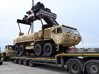 A crane lifts and moves a U.S. Army vehicle to the truck after offloading from the cargo v