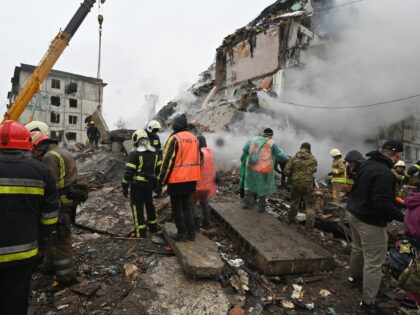 Firefighters work next to people cleaning rubble of a building following a missile strike