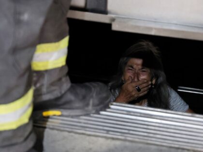 An elderly person trapped in an elevator reacts as firefighters assist in her rescue durin