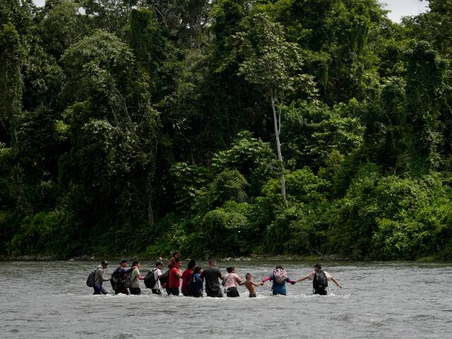 Migrants wade hand in hand as they cross the Tuquesa River, near Bajo Chiquito, Panama, af