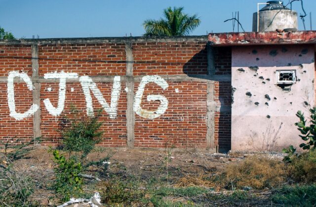 The initials of the Jalisco New Generation Cartel (CJNG) are seen on a bullet-riddled wall