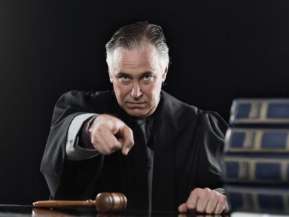 Judge in a legal robe glares at the camera and points with his index finger.