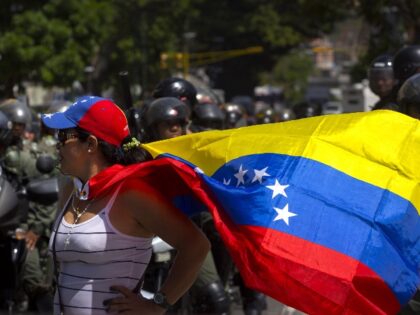 A woman wearing Venezuela's flag as a cape protests as police stand guard in Caracas, Vene