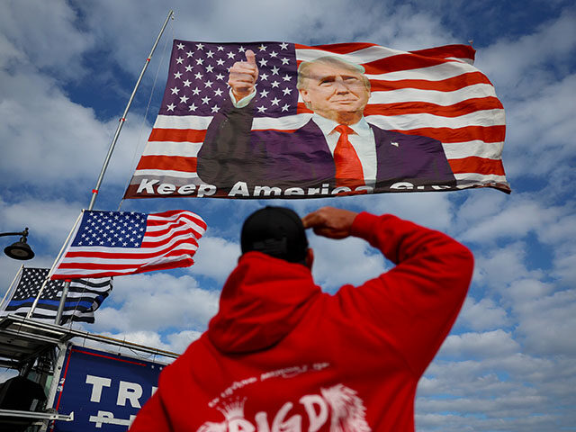 Derek Arnold salutes a flag featuring former President Donald Trump that supporters are fl