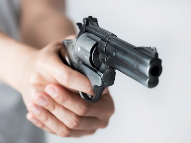 Unrecognizable person wearing a grey t-shirt is holding a gun with two hands in front of g