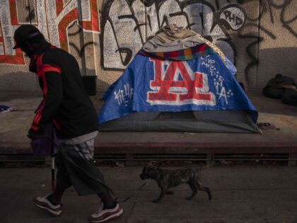 FILE - A man walks past a homeless encampment in downtown Los Angeles, Wednesday, Oct. 25,