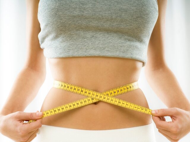 a woman checks her waist size with a measuring tape