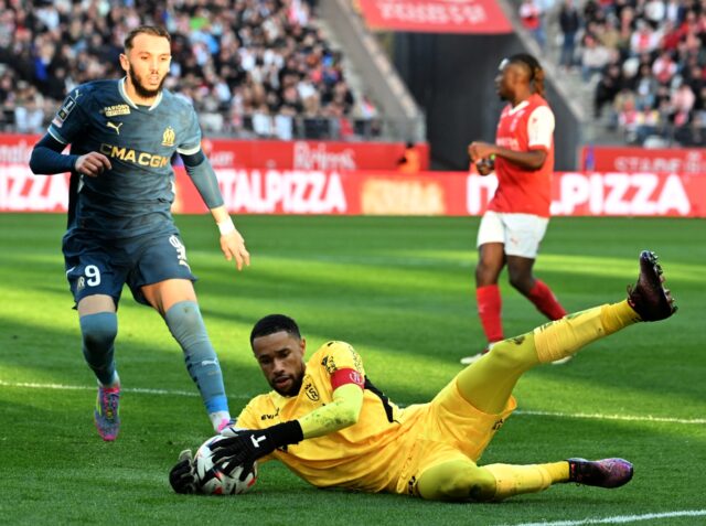 Reims goalkeeper Yehvann Diouf (C) gathers the ball as Marseille's Amine Gouiri (L) looks
