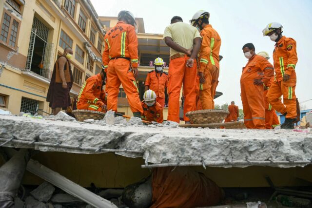 Rescue workers try to retrieve the body of a victim trapped in the rubble of a damaged mon