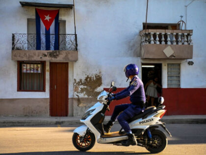 A police officer rides a motorbike in front of a house displaying a Cuban flag in Havana,