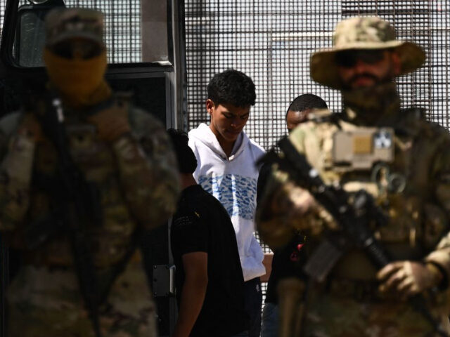 Texas Army National Guard look on as migrants board a bus after surrendering to US Customs
