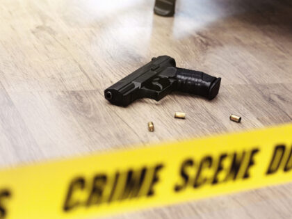 Crime scene tape in front of a handgun and spent cartridge cases lying on a wooden floor.