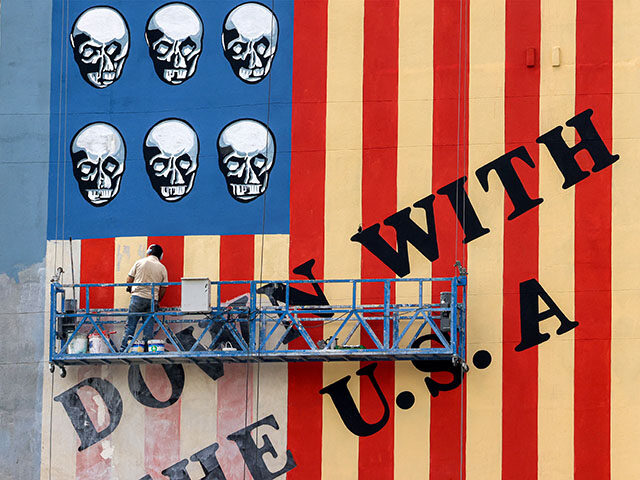 A man on a platform applies a fresh coat of paint to the landmark anti-US mural drawn on t