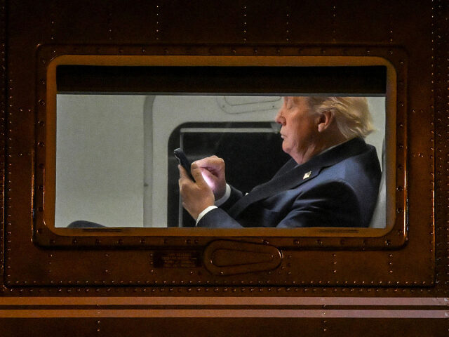 GettyImages-2211177567 US President Donald Trump uses a cellphone aboard Marine One before it departs Leesburg Ex