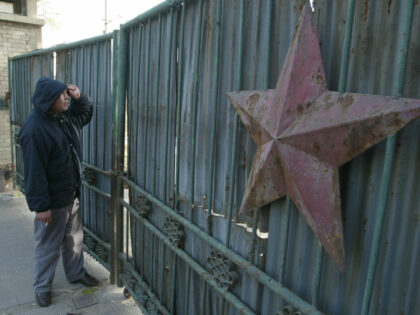 A taxi driver looks through the locked and dilapidated gate of a former State Owned Enterp