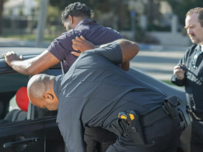 man in gray t-shirt being searched by two police officers