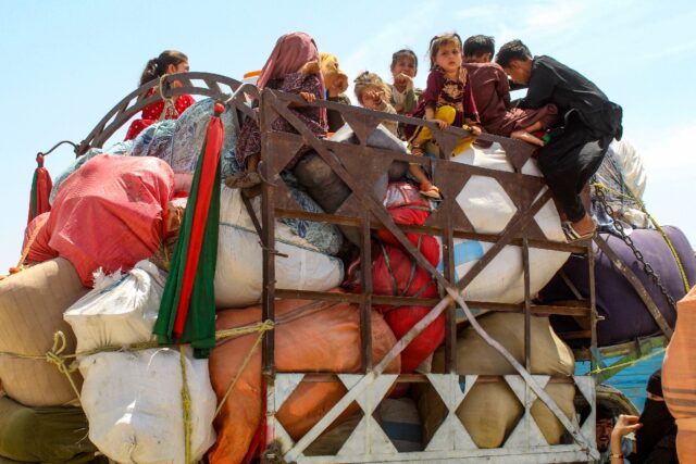 Afghan refugee children board a truck loaded with their belongings as they wait for their