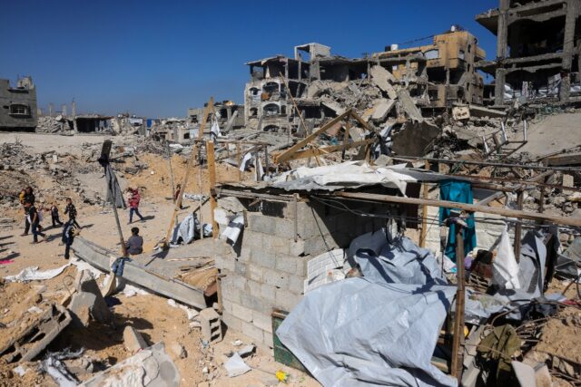 Children gather near a destroyed makeshift shelter following an Israeli strike in Beit Lah