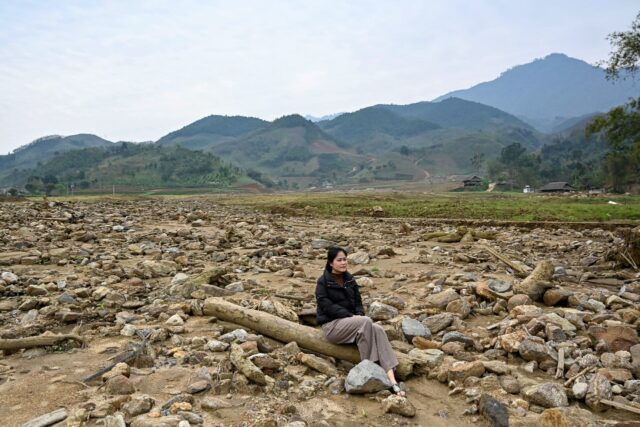 Nguyen Thi Kim sitting on a pillar of a destroyed house at the original site of Lang Nu vi