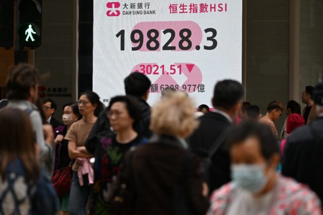 Pedestrians walk past an electronic sign board showing the closing price of the Heng Seng