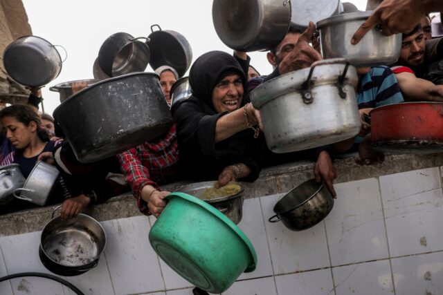 People crowd to receive charity meals from a kitchen in Beit Lahia, northern Gaza, as aid