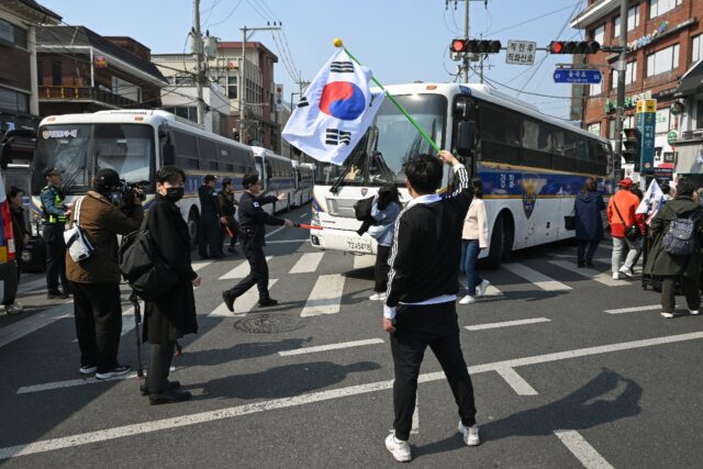 A man waves a South Korean flag as police buses block the road in front of the Constitutio