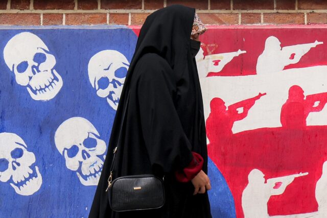 A woman walks past a mural on the walls of the former US embassy building in Tehran, known