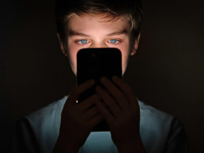 In this photo illustration, a teenage child looks at the screen of a mobile phone on Janua