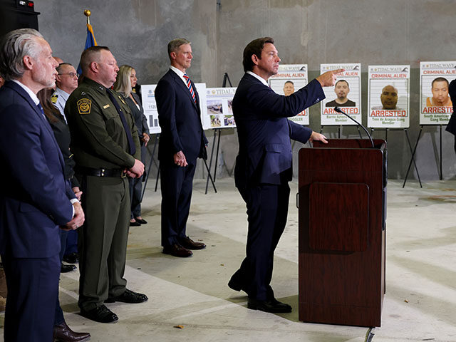 Florida Gov. Ron DeSantis speaks during a press conference, in front of posters of people