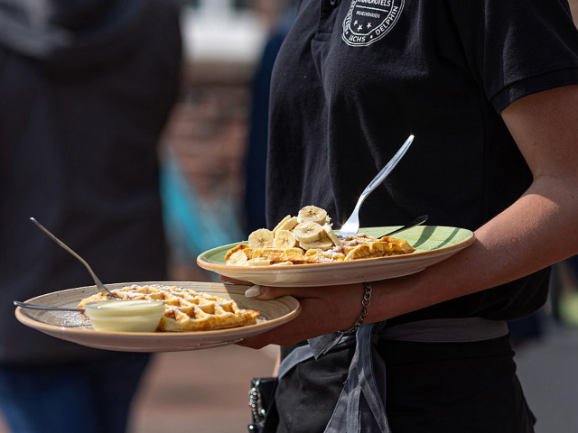 A waitress carries waffle desserts at a restaurant's terrace in Wilhelmshaven, Germany, on
