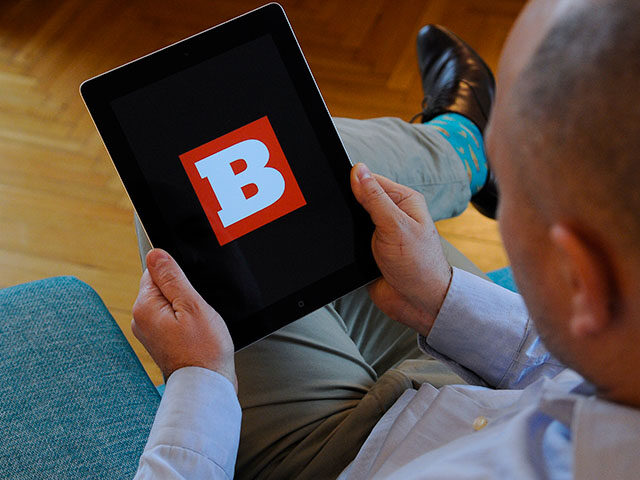 A man holds an iPad with the Breitbart logo on it's screen