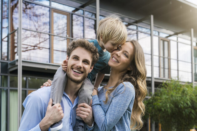 Germany, portrait of smiling family of father, mother and cute toddler boy standing in gar