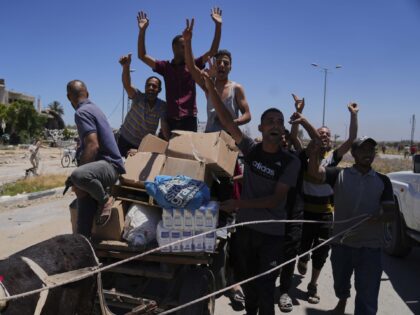 Palestinians wave to the camera as they carry boxes and bags containing food and humanitar
