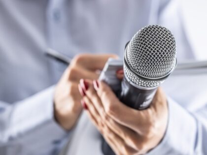 A journalist holds a microphone at a press conference and writes information in a notebook
