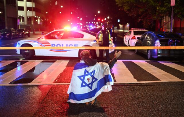 A man draped in the Israeli flag, bearing a cross and the name "Jesus" at its center, gest