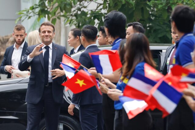 France's President Emmanuel Macron is greeted by flag waving university students in Hanoi