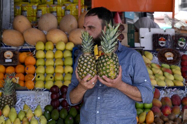 A man holds two pineapples at a stall selling fruits, many of which were not available whi